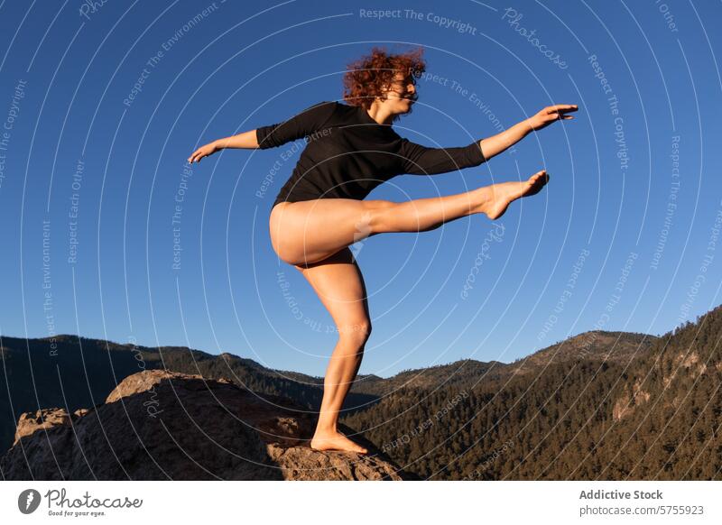 Graceful contemporary dancer balancing on a rock balance poise female blue sky forest mountain grace performing arts nature outdoor flexibility stretch pose