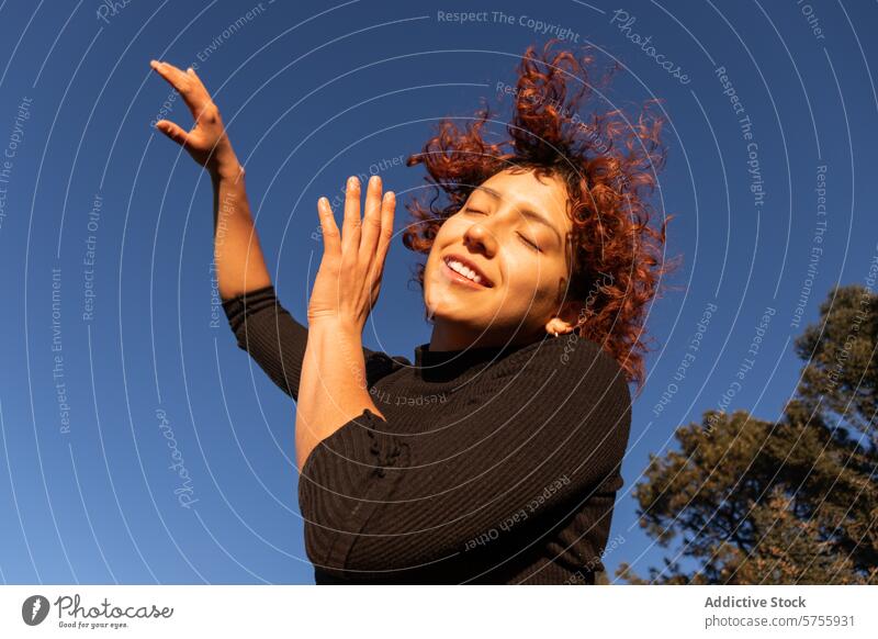 Joyful contemporary dancer under clear blue sky woman graceful red hair curls sunlight artistic expression culture outdoor natural light leisure hobby active