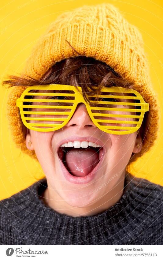 A girl radiates joy as she poses in vibrant yellow shutter shades and a matching beanie, set against a lively yellow background sunglasses fun smile fashion