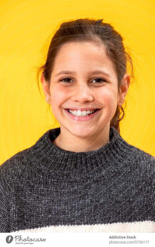 Portrait of a happy young girl with a bright smile, wearing a cozy sweater, set against a vivid yellow background portrait cheerful youth child teeth joy