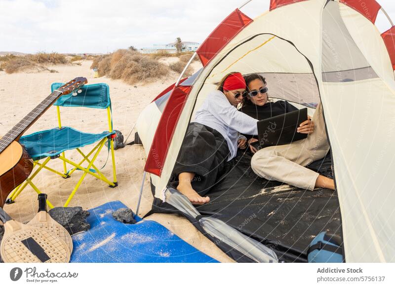 A couple relaxes inside their tent with a digital tablet, comfortably blending technology with their beach camping experience relaxation leisure woman sand