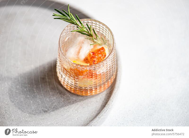 A crafted vodka tonic cocktail adorned with grapefruit and rosemary, resting on a textured tray for an upscale serving experience drink beverage ice garnish