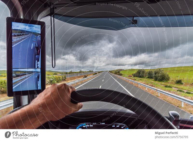 View from the driver's seat of a truck of an empty highway under a threatening sky of rain, truck with a rearview mirror for a camera. road transport