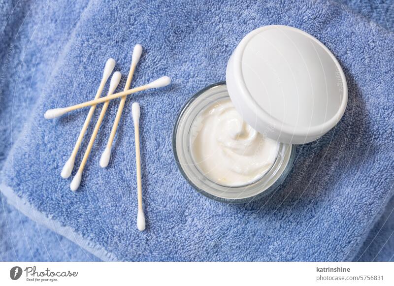 Opened cream jar with white lid near cotton swabs on blue towel top view, cosmetic mockup hygiene blank Brand packaging eco friendly organic skin care body care