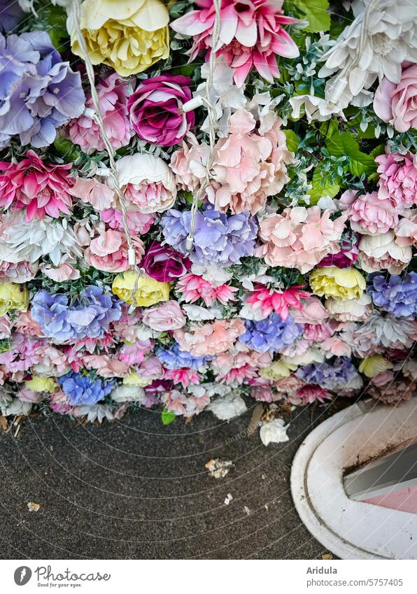 Artificial flower wall at the roadside tawdry Yellow carpet of flowers Violet purple White Pink Trashy Kitsch Plastic Blossoming artificial flowers Asphalt