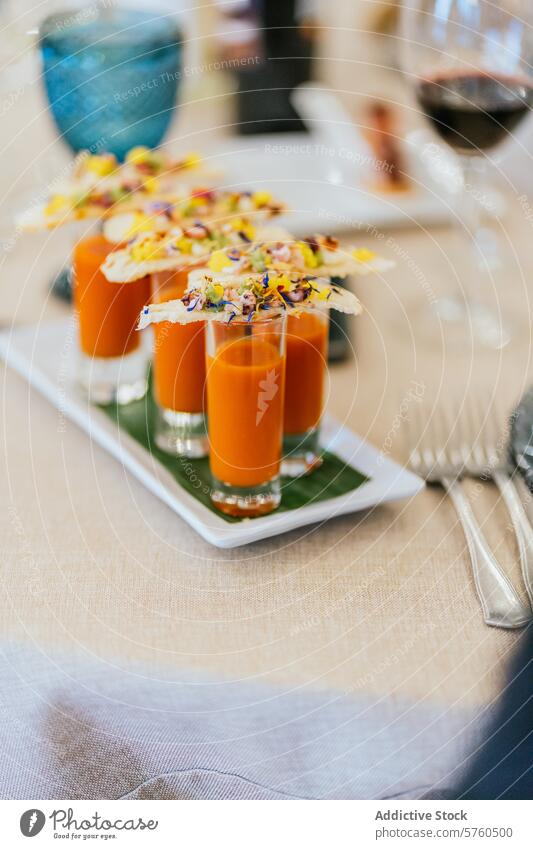 An artistic display of orange soup shooters topped with lavishly garnished crackers on an elegant dinner table setting cuisine appetizer catering event culinary