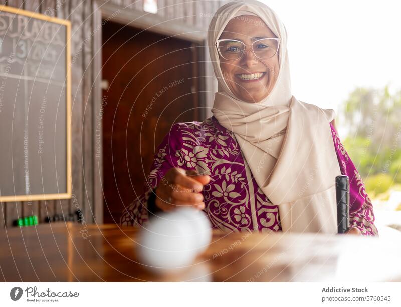 Joyful muslim woman enjoying a game of mini golf cheerful smiling golf ball golf club leisure activity sport recreation happiness glasses enjoyment headscarf