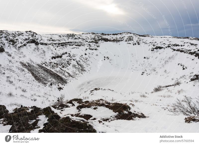 An expansive view of a snow-filled crater in Iceland, with rugged terrain surrounding the icy depression under a cloudy sky snowy Icelandic wilderness landscape