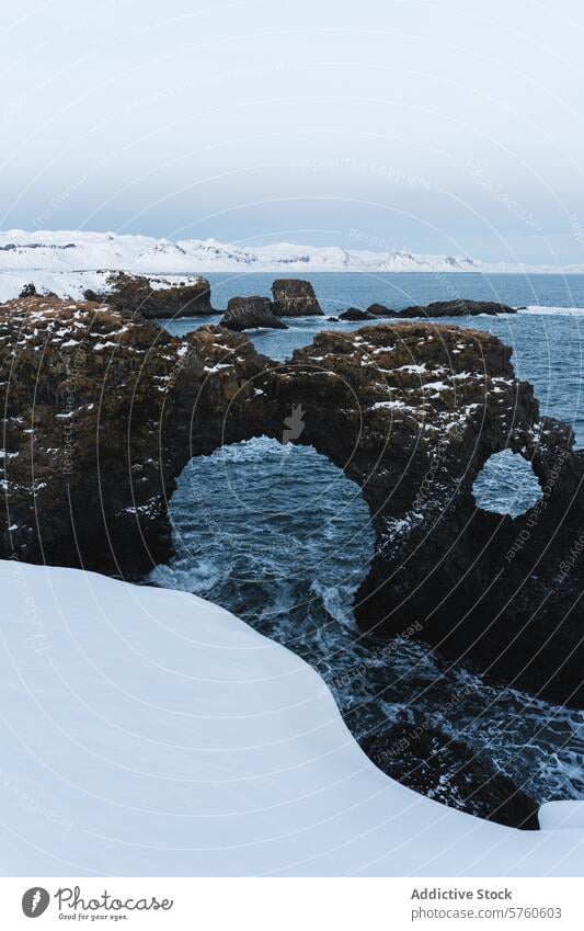 The natural arch of volcanic rock stands amidst the snow and turbulent waters along the starkly beautiful coast of Iceland winter archway Icelandic seascape
