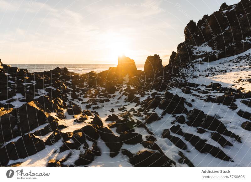 The setting sun casts a warm glow over the rugged, snow-spotted rocks of an Icelandic shore, creating a stark and beautiful contrast sunset winter nature