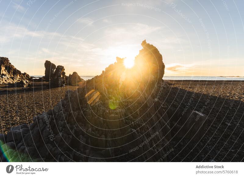 A captivating sunburst peaks through the unique rock formations on a pebbled Icelandic beach, creating a dramatic start to the day sunrise nature landscape