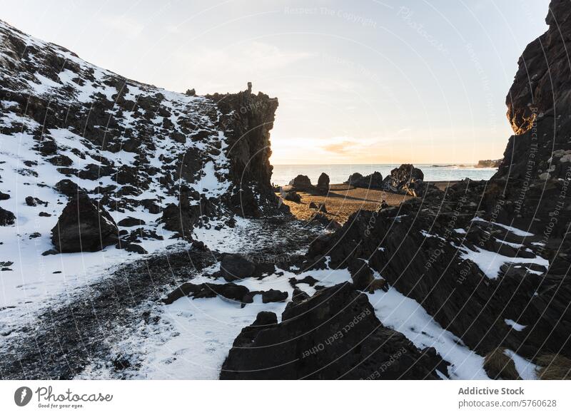 The golden glow of sunrise bathes the unique rock formations and snow-patched cliffs along an Icelandic beach, showcasing nature's contrasts snowy landscape