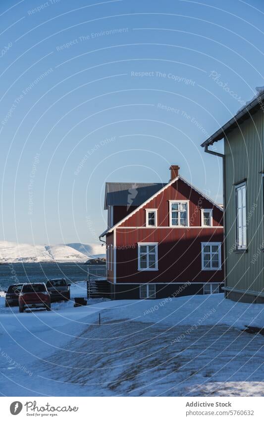 A traditional Icelandic red house stands proudly against a vast mountain range, under the crystal-clear blue skies of a cold winter day home backdrop blue sky