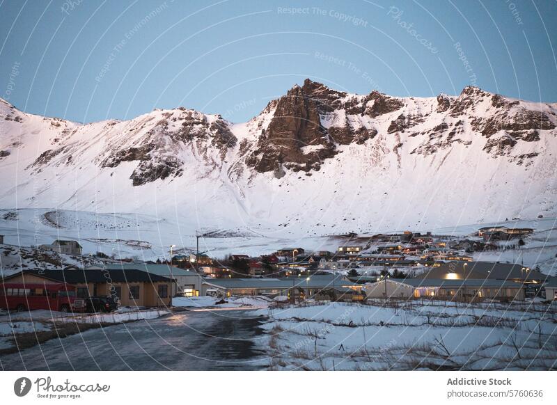 A cozy Icelandic village nestles at the foot of towering, snow-capped mountains, illuminated by the soft glow of dusk twilight landscape nature travel scenic