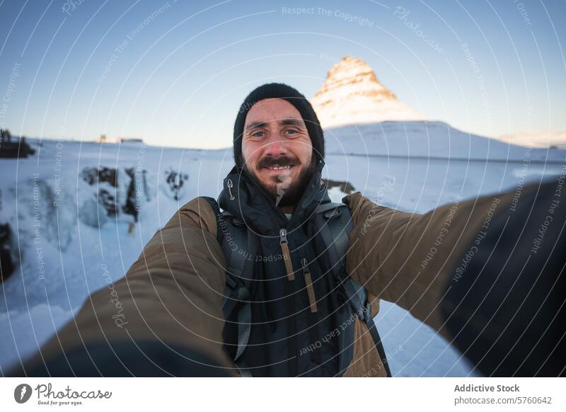 A bearded traveler captures a selfie moment with the sunlit Kirkjufell mountain, a famous Icelandic landmark, in the snowy background man adventure tourism