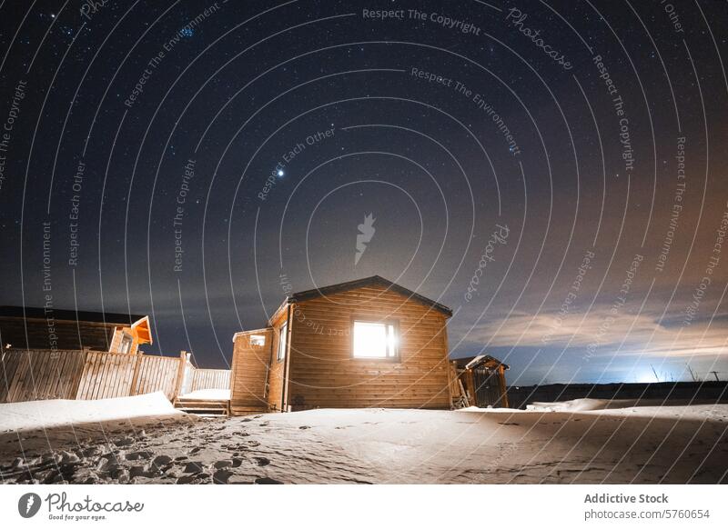 A cozy wooden cabin in Iceland, illuminated against a starry night sky, offers a warm haven amidst the snowy landscape winter outdoor shelter travel Nordic