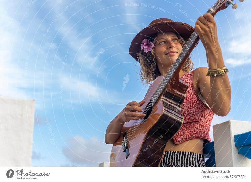 Female musician playing guitar outdoors in urban setting woman street culture passion hat flower hair performance artistic hobby leisure sky city town performer