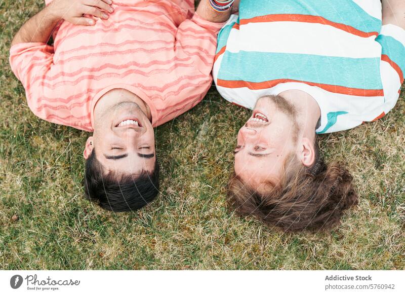 Top view of two men, a couple in love and both transgender, share a moment of pure joy and laughter while lying on the grass gay happiness smile relationship