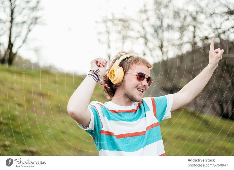 A cheerful man with a broad smile and yellow headphones raises his hand in joy while dancing in a serene outdoor setting joyful music celebration enjoyment