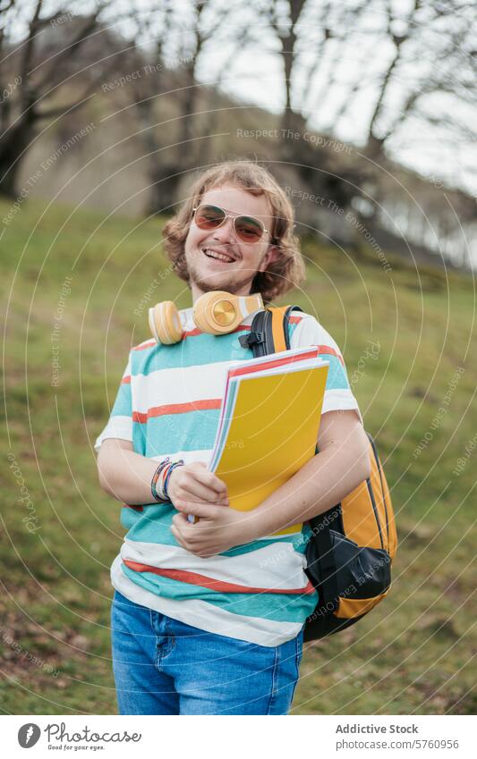 A cheerful student with curly hair and sunglasses, holding notebooks and wearing headphones, stands outdoors with a backpack happy education study casual