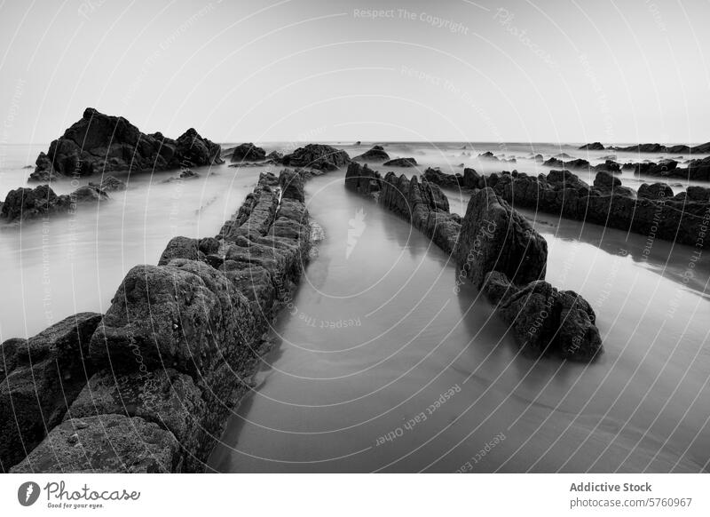The textured rocks of Playa de Barrika stand stark against the smooth sea in this dramatic black and white coastal scene near Bilbao monochrome mystery shore