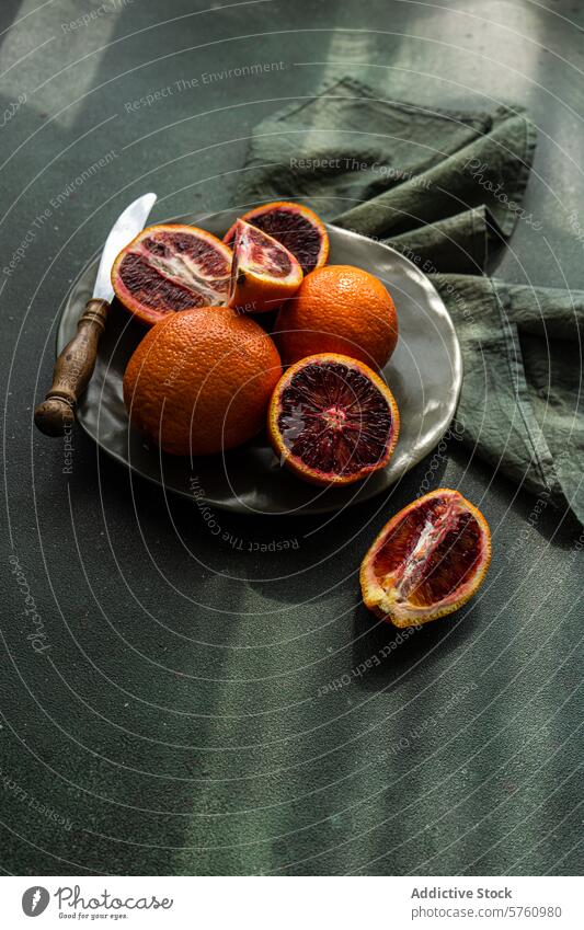 Rustic blood oranges setup on dark background fruit plate rustic knife green cloth citrus fresh cut food photography healthy vitamin c whole halved juicy shadow