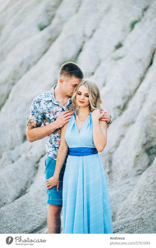 blonde girl in a light blue dress and a guy in a light shirt in a granite quarry boyfriend young teenager for a walk together gravel heap gray sand mountains