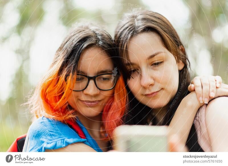 Two young girls hug each other while looking at the mobile phone to take a selfie female person women friendship portrait lifestyle outdoors together two adult