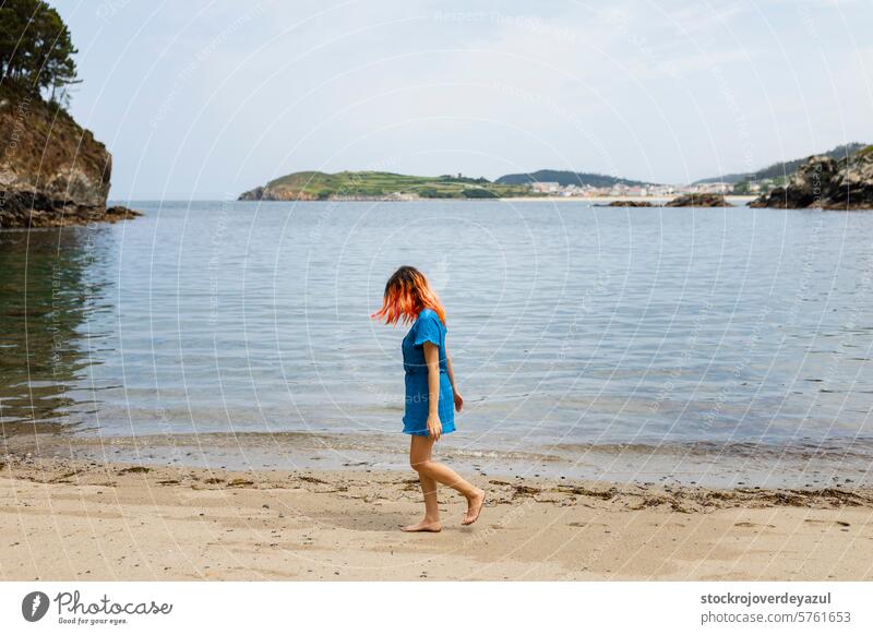 A young girl with orange hair strolls calmly along the seashore on a natural beach in northern Galicia ocean woman summer walking desclza galicia female water