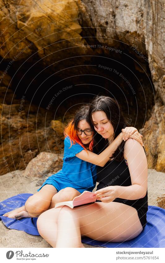 A couple of girls in love enjoy each other cuddling reading book on the beach on a summer day person friendship lifestyle young two females women together