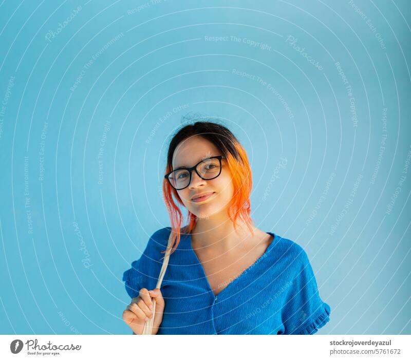 A young girl with orange hair looks at the camera with a smile, on a plain blue background woman female beauty person happy attractive adult real people galicia