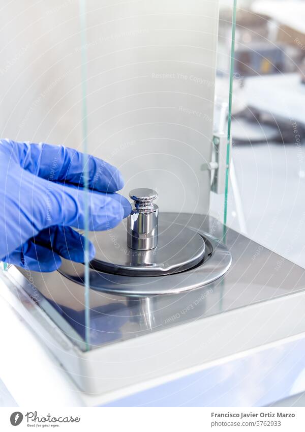 A operator's hand is holding steel calibration weight to place on the analytical balance. Concept of quality control in a laboratory. scale globes pharmacy