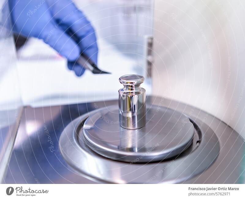 A operator's hand is holding steel calibration weight to place on the analytical balance. Concept of quality control in a laboratory. scale globes pharmacy