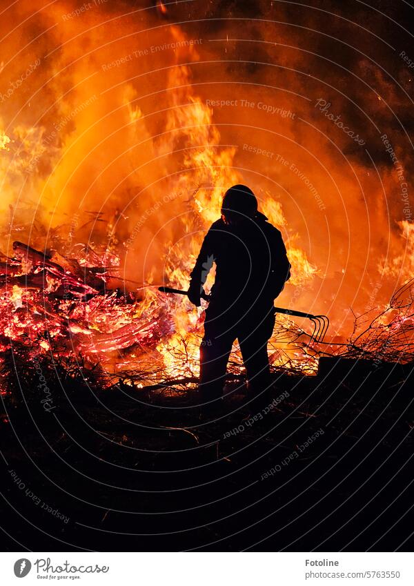 A fireman uses a fork to pull the wood from the edge into the flames so that all the evil spirits are driven away. ardor Fire Fireman Burn Hot Warmth Flame