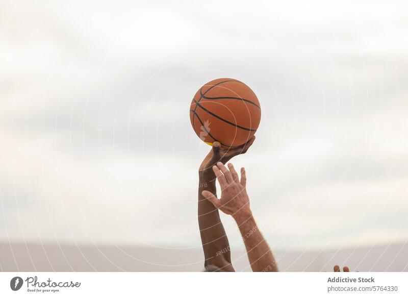 A basketball held steady in the hand of a player against a soft-focus background, ready for action on the outdoor court shot sport game sky preparation