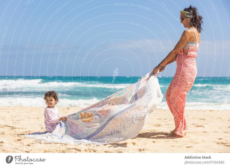 Mother and child playing with fabric on sunny beach family woman sand sea breeze summer outdoor leisure fun bonding mother daughter female toddler ocean coast
