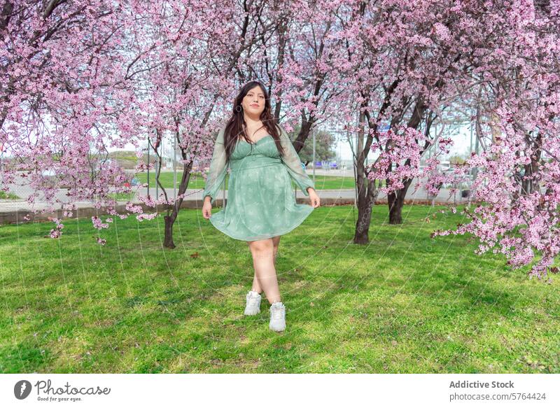 Woman in green dress enjoying cherry blossom season woman spring casual sneakers park nature outdoors blooming tree grass leisure floral fashion lifestyle