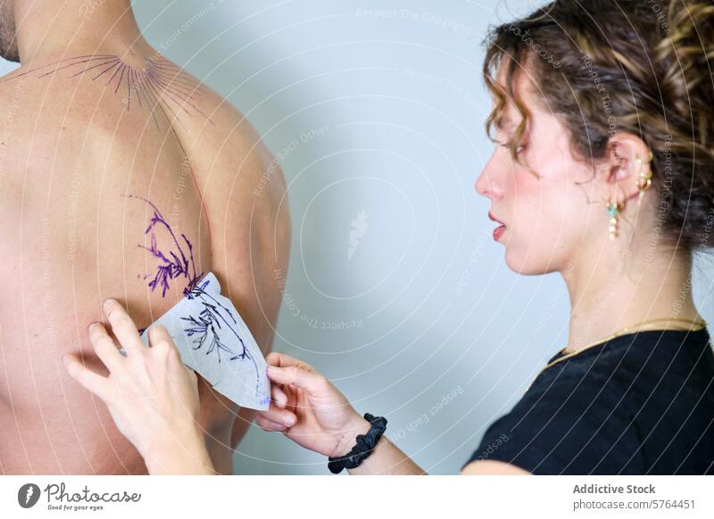 Tattoo artist applying design on client's back tattoo woman stencil floral preparation studio transfer skin body art ink tattooing professional creativity