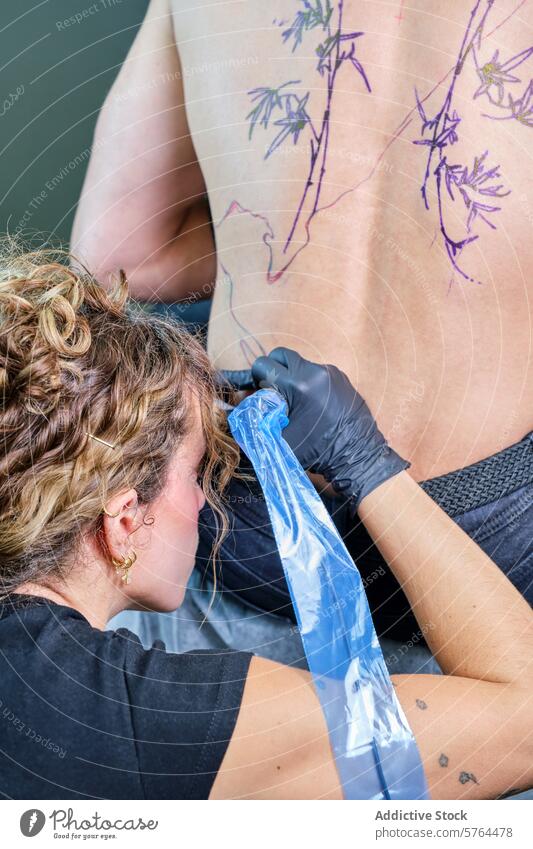 Female tattoo artist working on client's back in studio woman ink design professional creating tattooing process body art drawing detail skin needle glove