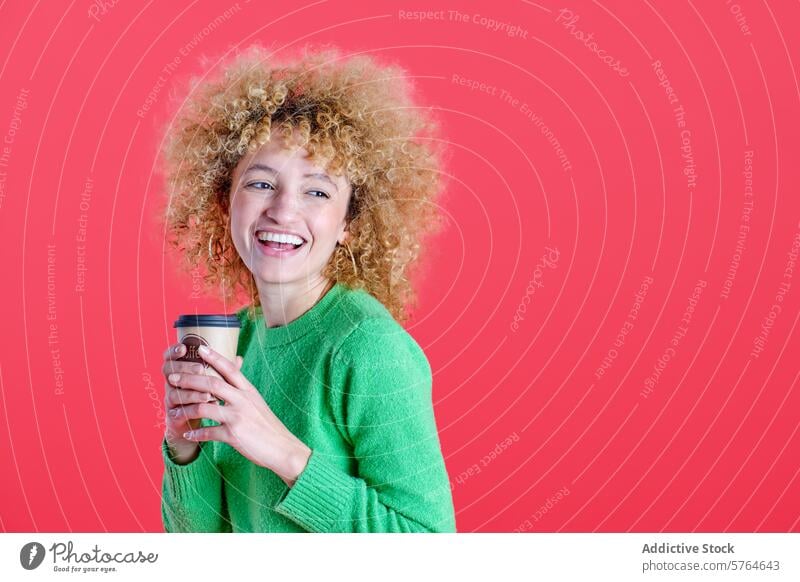A radiant woman with curly hair holds a coffee cup, her smile beaming, in a lush green sweater against a bold red backdrop red background beverage happy denim