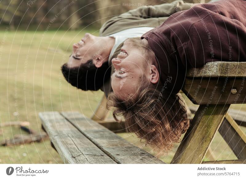 Upside-down view of a gay couple laughing together while lying back on a picnic bench, enjoying a playful moment in an outdoor setting shared laughter unique