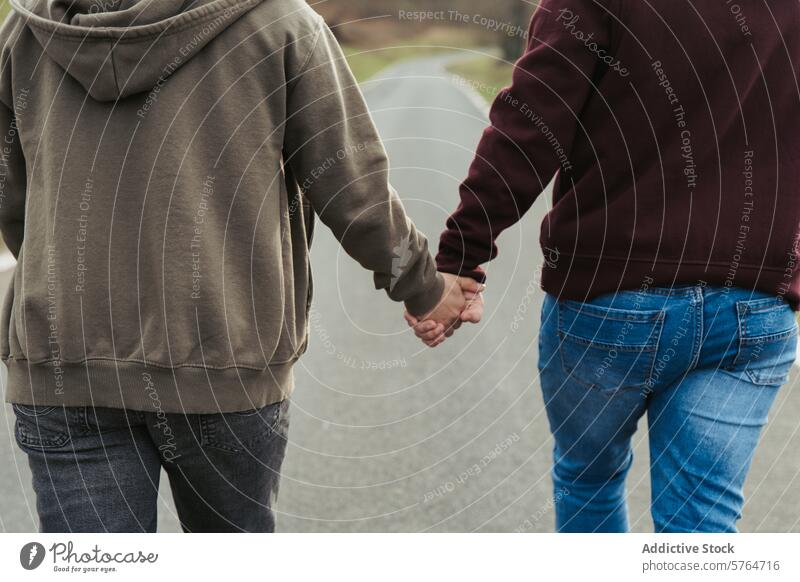 Close-up of anonymous couple holding hands, with a focus on their intertwined fingers, symbolizing love and connection on a quiet walk road close-up
