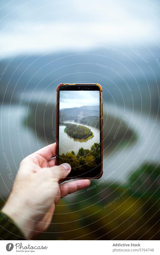 Capturing a river meander through a smartphone screen hand trees mist framing picturesque nature scenery river bend outdoor holding capture peaceful landscape