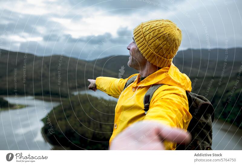 Adventurous man overlooking a river meander in winter adventure scenic landscape nature outdoor travel exploration hat raincoat yellow woolen hill forest