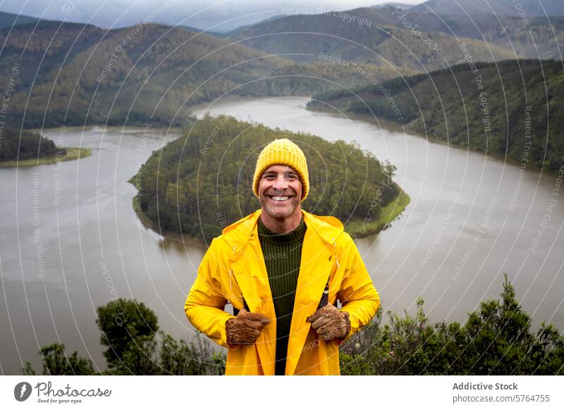 Man in Yellow Jacket Enjoying Scenic Winter River View man yellow jacket beanie smile river landscape winter adventure outdoor scenic travel nature cheerful