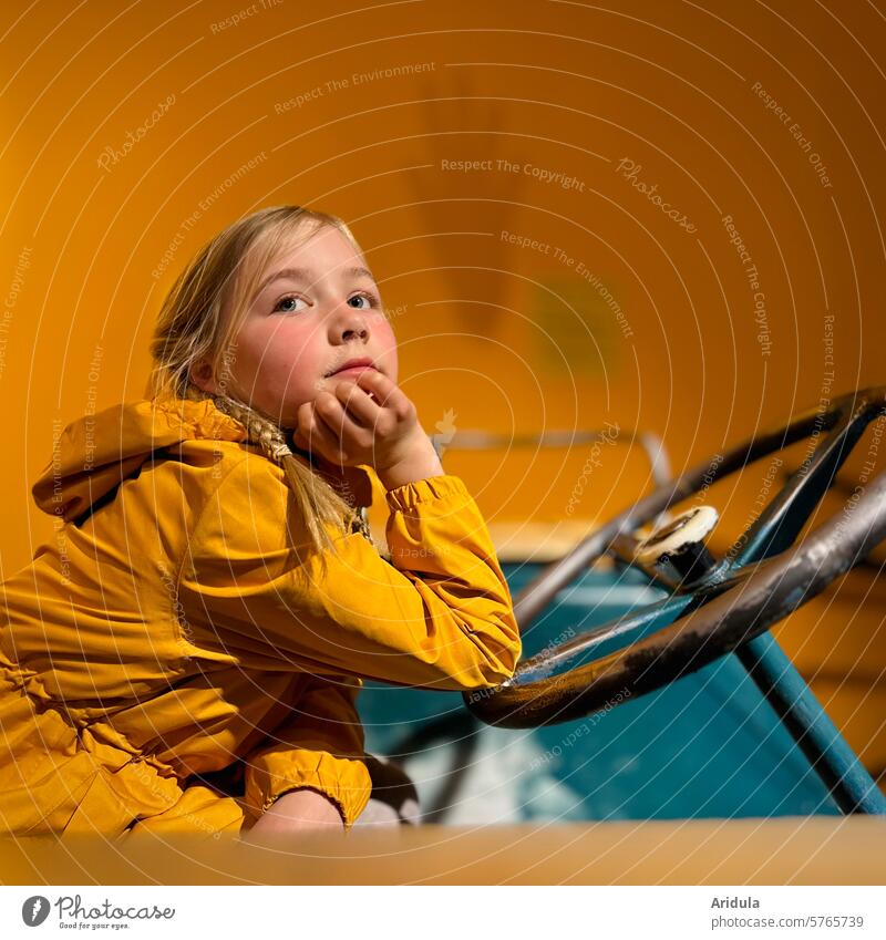 Girl sits on an old tractor and rests her face on her hand Child Dream ponder Meditative Yellow Rain jacket blonf plaits Infancy portrait Human being Dreamily
