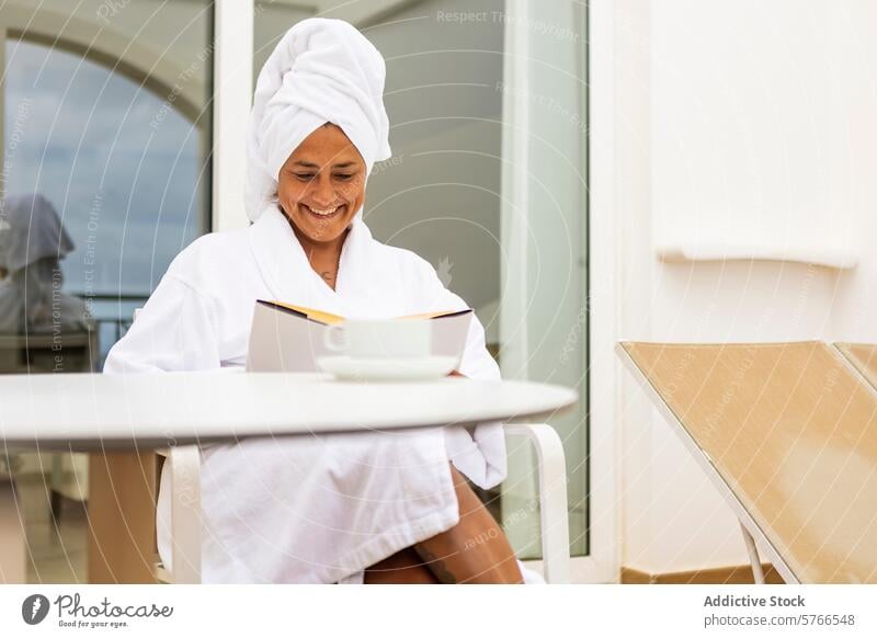 Middle aged hispanic woman in bathrobe enjoying a book and coffee on a balcony towel smiling reading relaxation morning leisure serene beverage peaceful outdoor