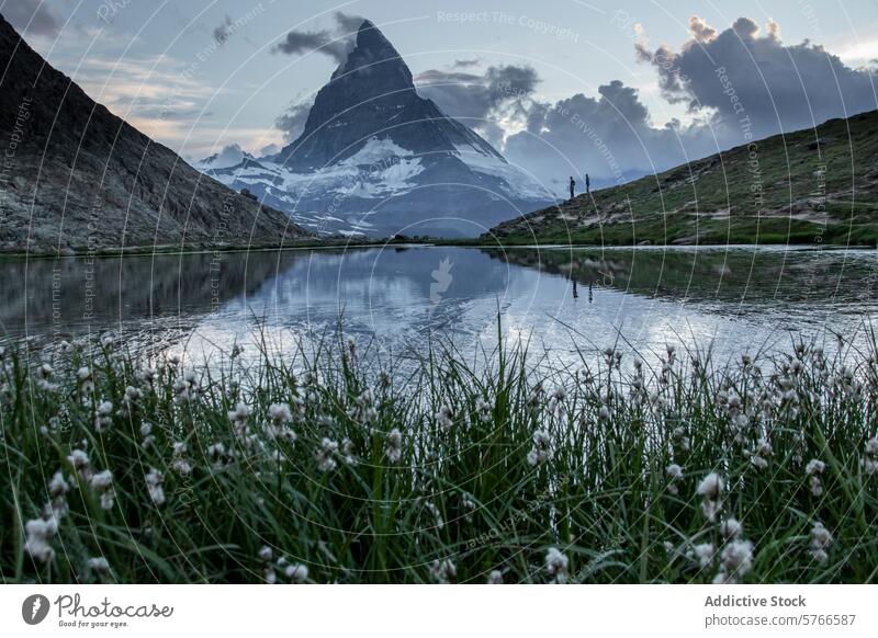 The majestic Matterhorn is mirrored in the still waters of a mountain lake at dusk, with onlookers in the distance adding scale to the scene reflection alpine