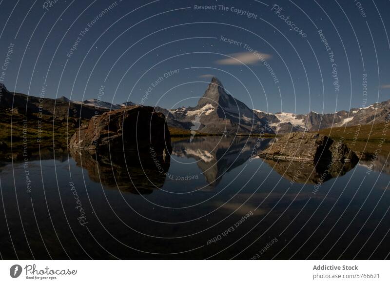 Under a starry sky, the Matterhorn is perfectly mirrored in the tranquil Stellisee, with a large boulder adding drama to the nocturnal Alpine landscape