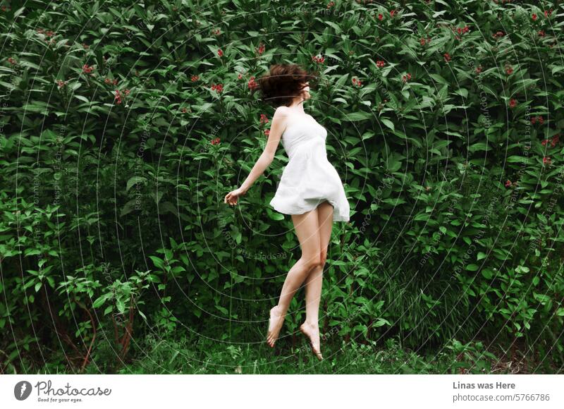 It’s all green outdoors. And a gorgeous brunette girl in a white dress is jumping for joy. Linas was here. Jump green nature long legs pretty legs beauty